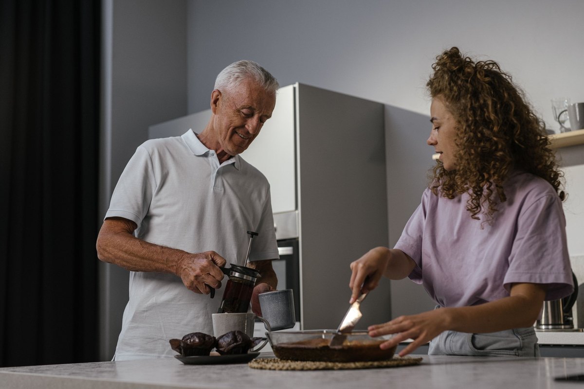 Older man and younger woman cooking and serving food together at a kitchen counter